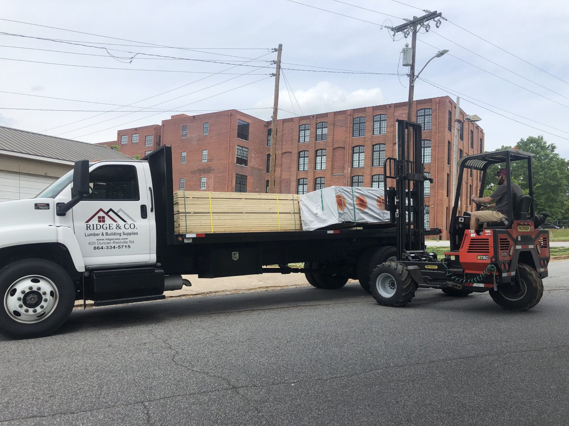 A Ridge & Co. flatbed truck loaded with framing lumber beside a piggyback forklift
