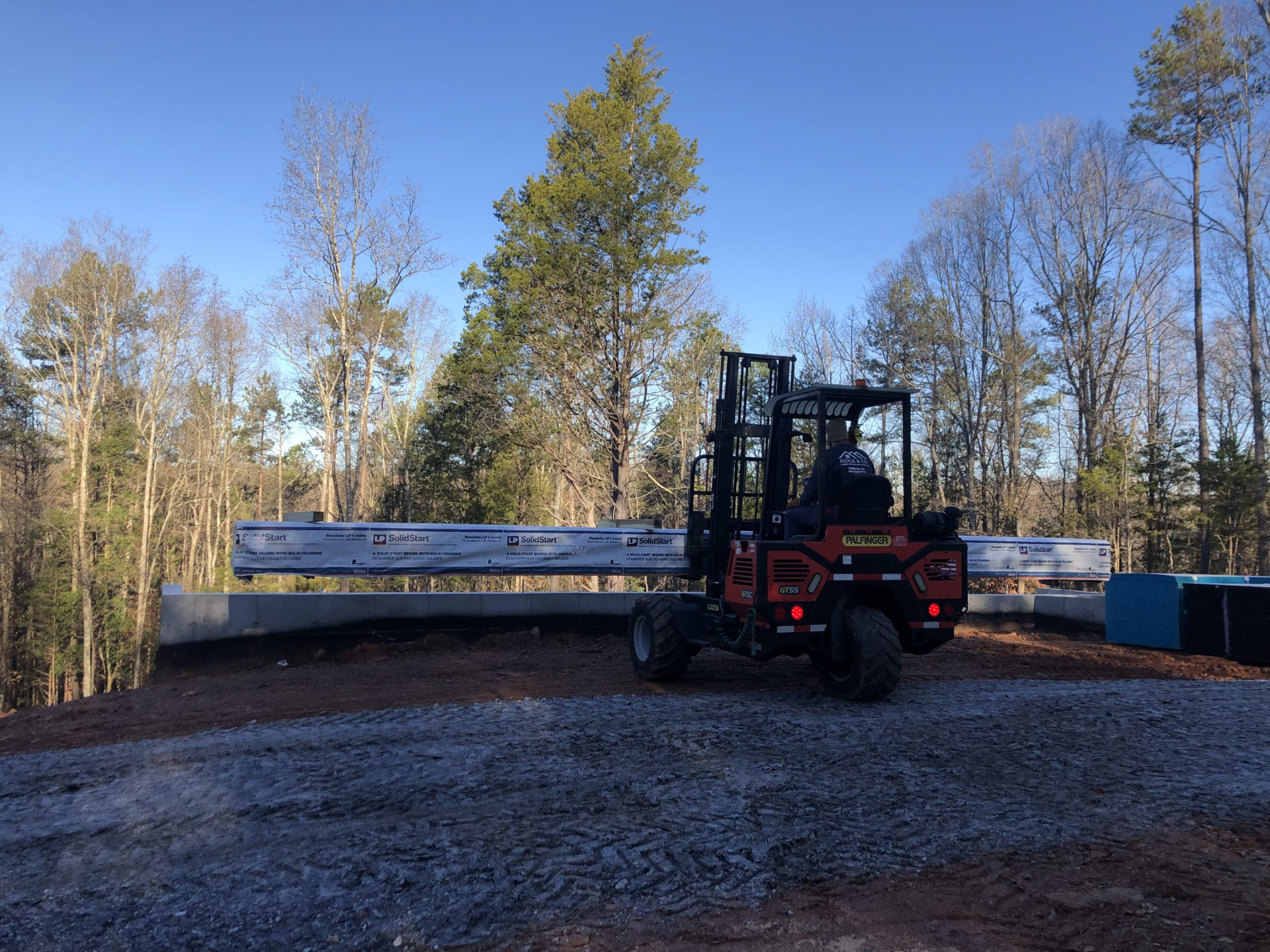 Piggyback forklift setting engineered floor joists on a jobsite foundation